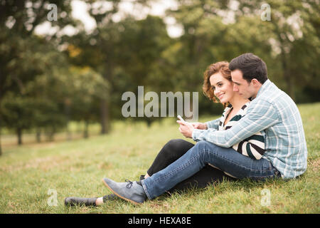 Couple sitting in field hugging looking at smartphone Banque D'Images