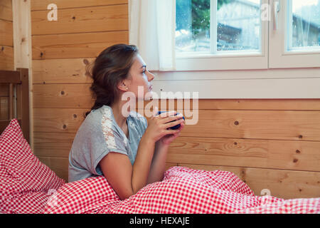 Jeune femme à la recherche d'une fenêtre de log cabin bed, Tyrol, Autriche Banque D'Images