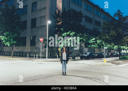 Portrait of young woman standing on city road junction at night Banque D'Images