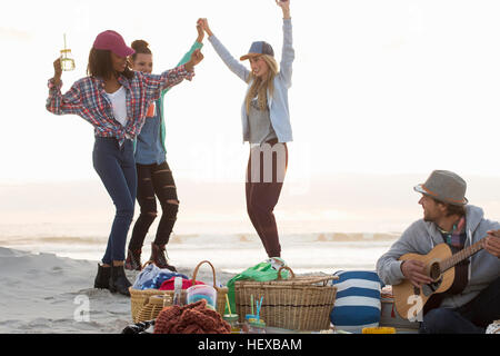 Jeune homme jouant de la guitare et amies de danse au Beach, Cape Town, Western Cape, Afrique du Sud Banque D'Images