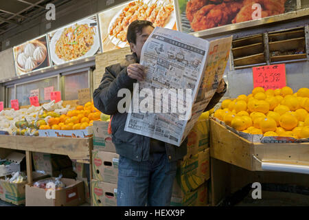 Une asiatique anonyme lire un journal quotidien près d'un stand de fruits en plein air dans le quartier chinois, le centre-ville de Flushing, Queens, New York Banque D'Images