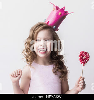 Belle petite princesse candy girl in crown holding big pink heart lollipop and smiling Banque D'Images