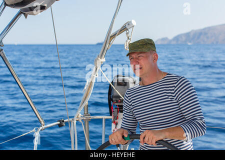 Jeune homme à la barre sur le bateau à voile. Les contrôles des navires pendant la course de la mer. Banque D'Images