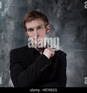Jeune homme en veste pensivement l'air dans l'appareil photo, la main sur le menton Banque D'Images