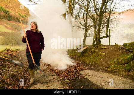 Llangynog, Powys, Wales, Royaume-Uni Le mardi 27 décembre 2016 par un froid glacial et matin dans Llangynog, un petit village au fond des montagnes Berwyn, au nord du Pays de Galles, KATE JEFFRIES, balaie et brûle les dérives de feuilles sèches qui se sont accumulés sur la piste de sa ferme à distance après le coup de vent et des tempêtes au cours de Noël Photo © Keith Morris / Alamy Live News Banque D'Images