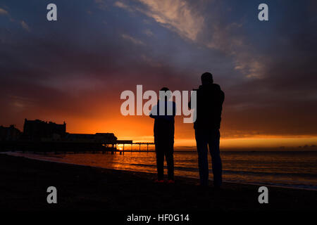 Pays de Galles Aberystwyth UK, le mardi 27 décembre 2016 UK weather : à la fin d'une claire et très froide journée de décembre, un père et son fils photographies les dizaines de milliers d'étourneaux qu'ils effectuent sur murmurations dramatique avant de descendre à Aberystwyth foule ensemble et se percher pour la nuit en toute sécurité sur les jambes de fer de fonte sous la ville balnéaire victorienne pier Bien qu'apparemment abondante à Aberystwyth, les oiseaux sont dans la RSPB's 'red' liste des espèces en péril, avec leur nombre à travers le Royaume-Uni a diminué de plus de 60  % depuis les années 1970, Photo © Keith Morris / Alamy Live News Banque D'Images