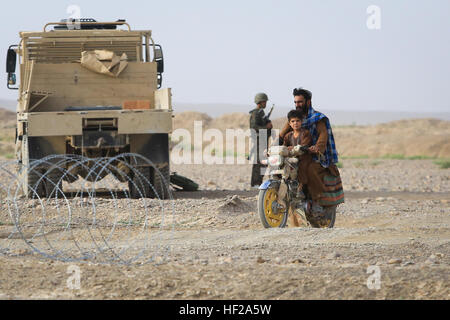 Les civils afghans ride passé une armée nationale afghane (ANA), soldat affecté à la 4e, 6e Kandak Tolay, 6e Brigade, 215e Corps, comme il fournit la sécurité pour un poste de contrôle des véhicules (VCP) dans le village Shekasteh Tappeh, province de Helmand, Afghanistan, le 14 juillet 2014. Soldats de l'ANA conduite VCP pour perturber l'activité de l'ennemi, de maintenir une présence militaire, et d'accroître la sécurité. (Official U.S. Marine Corps photo par Lance Cpl. Darien J. Bjorndal, Marine Expeditionary Brigade/ Afghanistan HELMAND) Parution-4ème Carmina fonctionne VCP, 140714-M-MF313-060 Banque D'Images