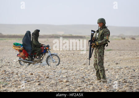 Les civils afghans ride passé une armée nationale afghane (ANA), soldat affecté à la 4e, 6e Kandak Tolay, 6e Brigade, 215e Corps, comme il fournit la sécurité pour un poste de contrôle des véhicules (VCP) dans le village Shekasteh Tappeh, province de Helmand, Afghanistan, le 14 juillet 2014. Soldats de l'ANA conduite VCP pour perturber l'activité de l'ennemi, de maintenir une présence militaire, et d'accroître la sécurité. (Official U.S. Marine Corps photo par Lance Cpl. Darien J. Bjorndal, Marine Expeditionary Brigade/ Afghanistan HELMAND) Parution-4ème Carmina fonctionne VCP, 140714-M-MF313-067 Banque D'Images