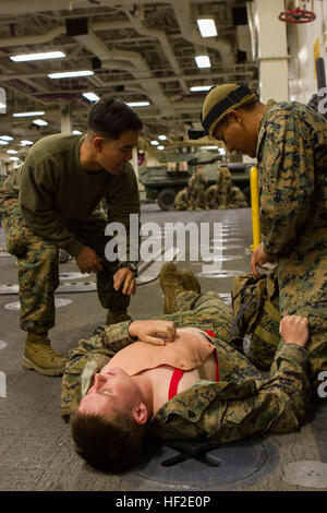 Maître de 2e classe Gabriel Besa, un instructeur de combat gareautrain avec des Groupe de travail Maritime Aérien Au sol, du Sud et originaire de Pearland, Texas, simule un environnement stressant en criant que le Cpl. Mike Zuni, un mécanicien en transport motorisé avec SPMAGTF-Sud et natif de Crownpoint, N.M., traite une plaie aspirante du thorax sur une victime simulée au cours de l'examen final d'un cours de combat à bord de l'avenir lifesaver navire d'assaut amphibie USS America (LHA 6), le 21 août, 2014. C'était le premier cours intégré de CLS à remplir au cours de l'équipage du navire de transport en commun. Les Marines et les marins ont appris se Banque D'Images