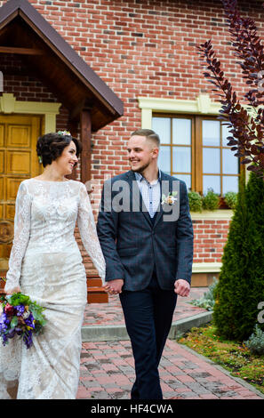 Couple de jeunes mariés marié et mariée passe à l'autre se tenant la main. Dans la cour autour de house en saison d'automne. Banque D'Images