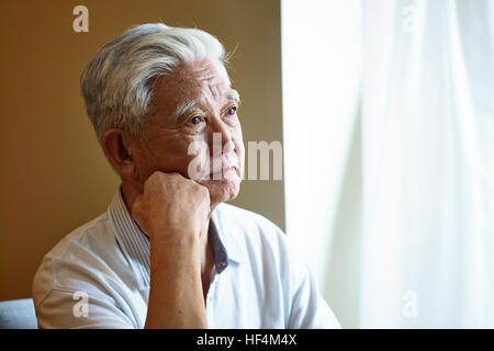 Portrait of a sad asian senior homme assis près de la fenêtre main sur le menton. Banque D'Images