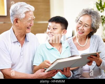 Heureux grand-père et grand-mère d'Asie la lecture d'un livre avec petit-fils, heureux et souriant. Banque D'Images