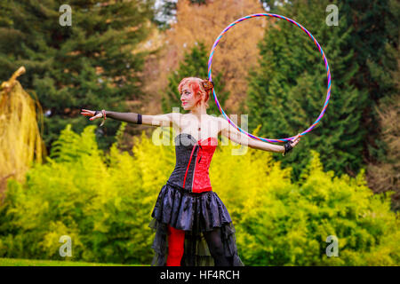 Belle jeune femme en costume de cirque jouer avec cerceau dans le parc. Banque D'Images