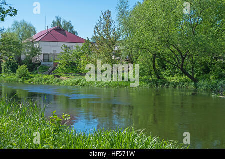 Une petite maison près d'une rivière entourée d'arbres printemps chaud jour Banque D'Images