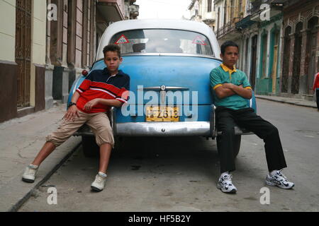 Deux garçons nonchalamment appuyé contre une voiture d'époque avec un couple dans le siège arrière, La Havane, Cuba, Caraïbes, Amériques Banque D'Images