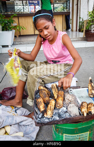 Une jeune fille philippine à Bogo City, île de Cebu aux Philippines les épis de maïs cuits sur charbon de bois à son emplacement sur le trottoir. Banque D'Images