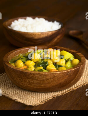 Curry de pois chiches Vegan ou chana masala aux épinards, pomme de terre et carotte servi dans bol en bois avec du riz à l'arrière Banque D'Images