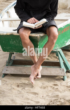 L'homme de lire un livre assis sur fishing boat on beach Banque D'Images