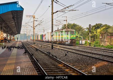 Train de marchandises de l'Indian Railways crossing une gare déserte sur un matin d'hiver brumeux. Banque D'Images