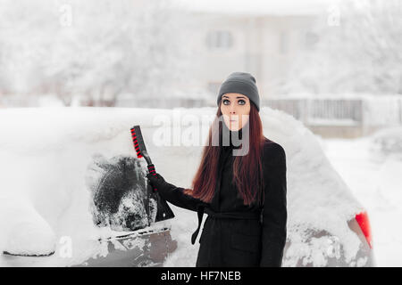 Femme drôle avec un pinceau enlever la neige de la voiture Banque D'Images