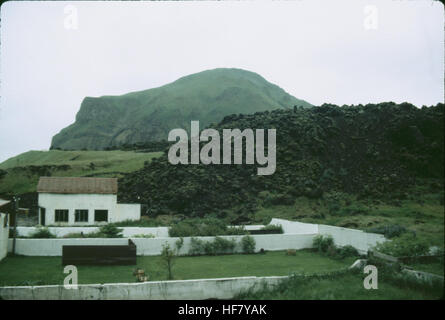 Cette photographie représente la coulée de lave de 1973 près d'un nouveau bâtiment sur l'île Heimaey, qui fait partie des îles Westmann en Islande, suite à l'éruption volcanique qui a menacé les infrastructures de l'île. Banque D'Images