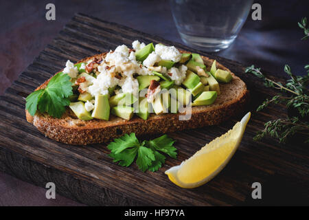 Collation santé avec avocat, fromage blanc, noix et d'huile d'olive sur le pain de blé entier grillé. Vue rapprochée, selective focus Banque D'Images