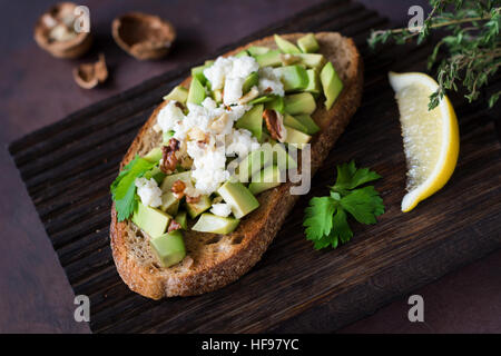 Collation santé avec avocat, fromage blanc, noix et d'huile d'olive sur le pain de blé entier grillé. Vue rapprochée, selective focus Banque D'Images