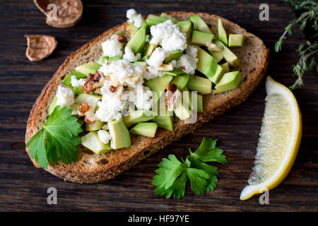 Collation santé avec avocat, fromage blanc, noix et d'huile d'olive sur le pain de blé entier grillé. Vue rapprochée, selective focus Banque D'Images