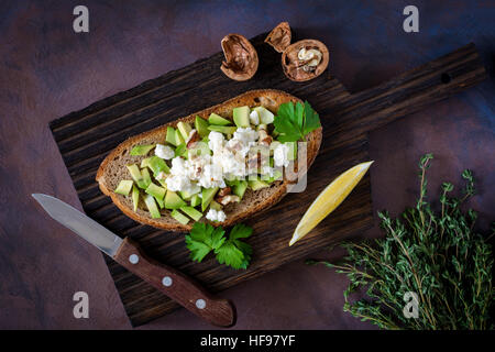 Collation santé avec avocat, fromage blanc, noix et d'huile d'olive sur le pain de blé entier grillé. Vue rapprochée, selective focus Banque D'Images