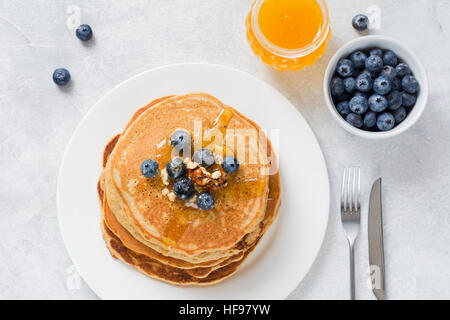 Pile de crêpes aux bleuets frais, noix et miel sur plaque blanche. Petit déjeuner santé alimentation. Banque D'Images