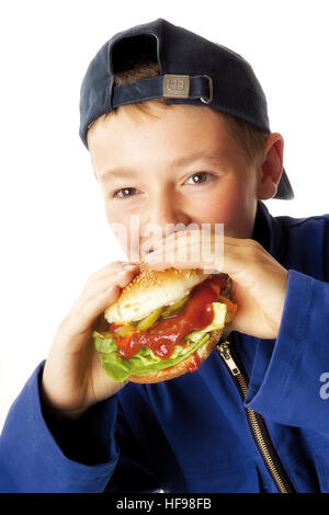 Jeune garçon portant salopette bleue mordre dans un hamburger Banque D'Images