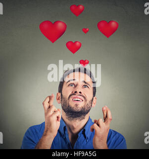 Jeune homme qui aime faire un souhait isolé sur fond gris avec coeur rouge au-dessus de la tête Banque D'Images