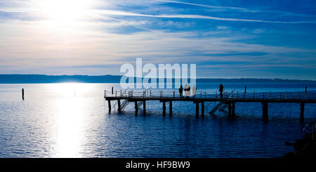 Pier sur la mer avec des gens sur elle, se découpant contre le soleil fort Banque D'Images