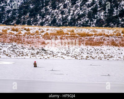 Pêcheur sur glace solitaire agenouillée à un trou dans la glace avec la canne à pêche Banque D'Images