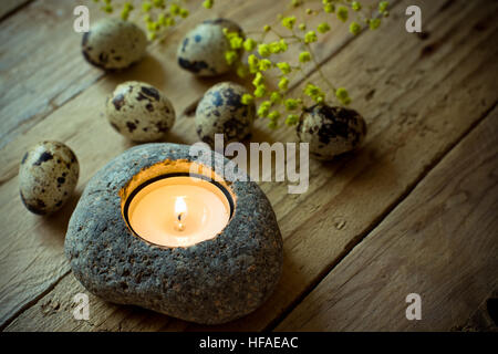 Oeufs de caille dispersés printemps délicates fleurs jaunes et un bougeoir en pierre avec plateau de lumière sur fond de bois vieilli, Pâques Banque D'Images