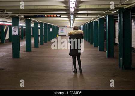 Jeune femme anonyme textos ou contrôler son téléphone portable sur un niveau vide NYC Subway à Greenwich Village, New York City, Banque D'Images