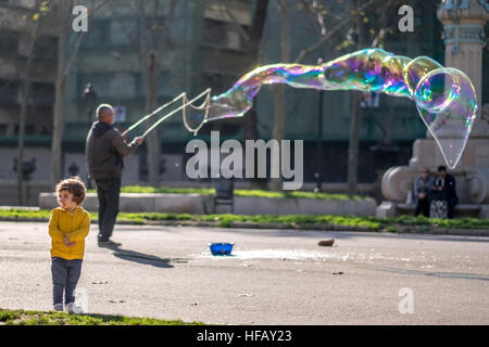 Un homme fait une bulle de savon géante dans un parc ensoleillé. Banque D'Images