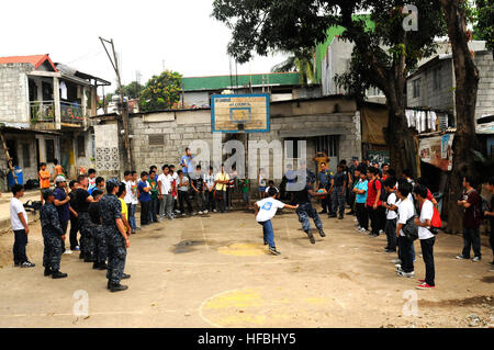 120201-N-OH194-104 MANILLE, Philippines (fév. 1, 2012) marins affectés à l'USS destroyer lance-missiles Wayne E. Meyer (DDG 108) regardez comme 1ère classe Mécanicien Mark Holbert joue au basket-ball avec un enfant de la région au cours d'un projet de service communautaire dans le village de collines Batasan situé dans la ville de Quezon article de Manille. Wayne E. Meyer, membre de l'USS John C. Stennis dans le groupe est déployé pour la 7ème Flotte américaine domaine de responsabilité la conduite d'opérations de sécurité maritime. (U.S. Photo par marine Spécialiste de la communication de masse 1ère catégorie de subvention P. Ammon/libérés) - Nav officiel aux États-Unis Banque D'Images