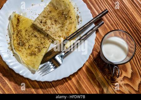 Crêpes crêpes au miel et noix dans une assiette et verre de lait sur une table en bois Banque D'Images