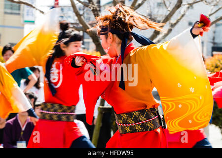 De Yosakoi. Jeune danseuse en orange et jaune veste yakata, danser et tout en souriant jaune tourbillonnant manches. Motion Blur. Banque D'Images