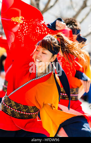 De Yosakoi. Jeune danseuse en orange et jaune veste yakata, danser et tout en souriant jaune tourbillonnant manches. Motion Blur. Banque D'Images