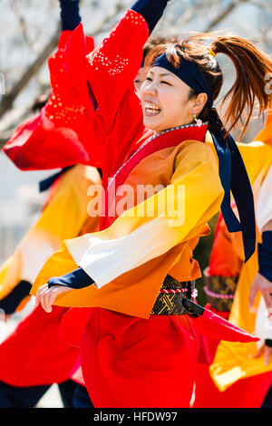 De Yosakoi. Jeune danseuse en orange et jaune veste yakata, danser et tout en souriant jaune tourbillonnant manches. Motion Blur. Banque D'Images