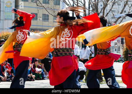 De Yosakoi. Jeune danseuse en orange et jaune veste yakata, danser et tout en souriant jaune tourbillonnant manches. Motion Blur. Banque D'Images