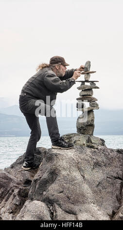 Homme d'empilage avec soin les roches dans un cairn, par la mer. Banque D'Images