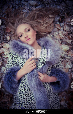 Modélisation photographique comme une carrière au Royaume-Uni : un jeune de 20 ans, slim woman femme fille avec de longs cheveux blonds allongée sur le dos sur le sol sur un jour froid froid comme une reine de glace Banque D'Images