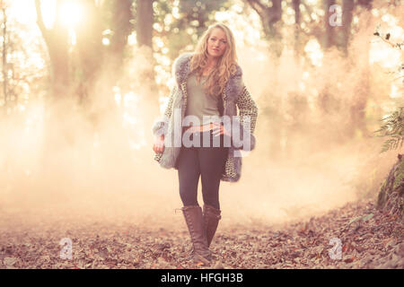 Modélisation photographique comme une carrière au Royaume-Uni : un jeune de 20 ans, slim woman femme fille avec de longs cheveux blonds marcher seule par elle-même dans les bois sur une chaude après-midi d'automne lumineux Banque D'Images