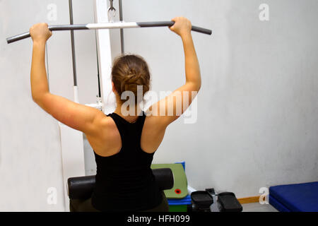 Femme à la salle de sport. L'élaboration de ses muscles du dos et des bras avec lat pulldown machine d'exercice. Banque D'Images