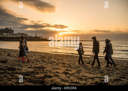 Pays de Galles Aberystwyth UK, New Years Eve, samedi 31 décembre 2016 UK weather : personnes marchant sur la plage au coucher du soleil sur la mer à Aberystwyth, sur la côte ouest du pays de galles sur le dernier jour de l'année. - La météo dans l'ouest a été clair, contraste fortement avec l'épais brouillard qui couvre une grande partie du sud-est de l'Angleterre photo : Keith Morris / Alamy Live News Banque D'Images