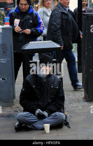 Manchester, UK. 31 Dec, 2016. Un homme assis à côté d'un bac sur une rue commerciale de Manchester, 31 décembre 2016 (C)Barbara Cook/Alamy Live News Banque D'Images