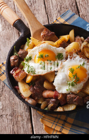 Pommes de terre frites tyrolien avec de la viande, du bacon et des œufs dans une casserole de près. La verticale Banque D'Images